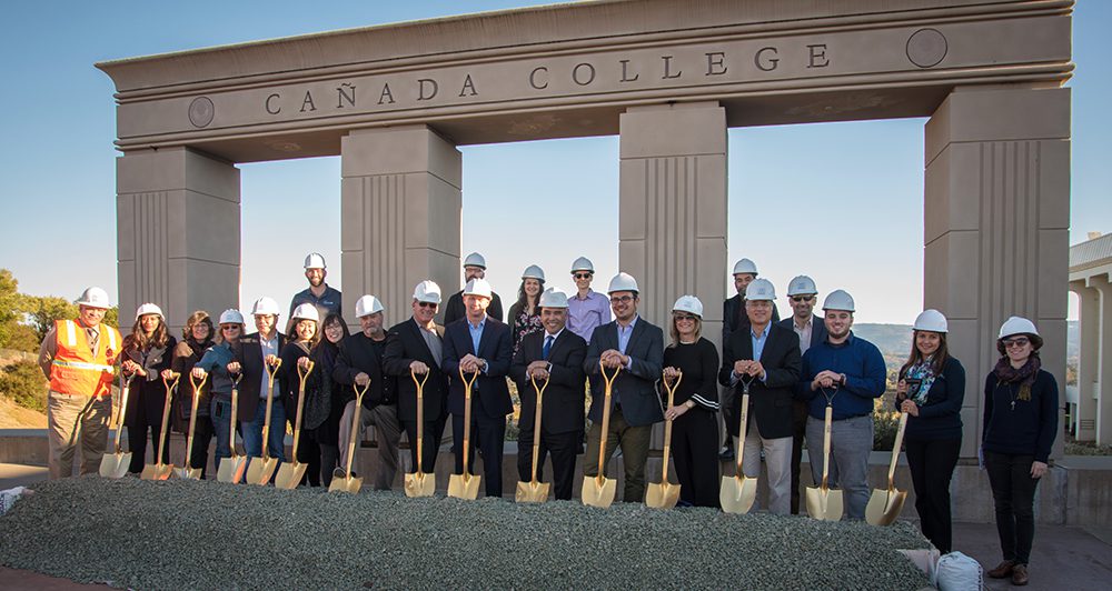 A crowd of people stand with golden shovels and hard hats at the groundbreaking ceremony for the Kinesiology, Wellness, and Aquatics Center at Cañada College